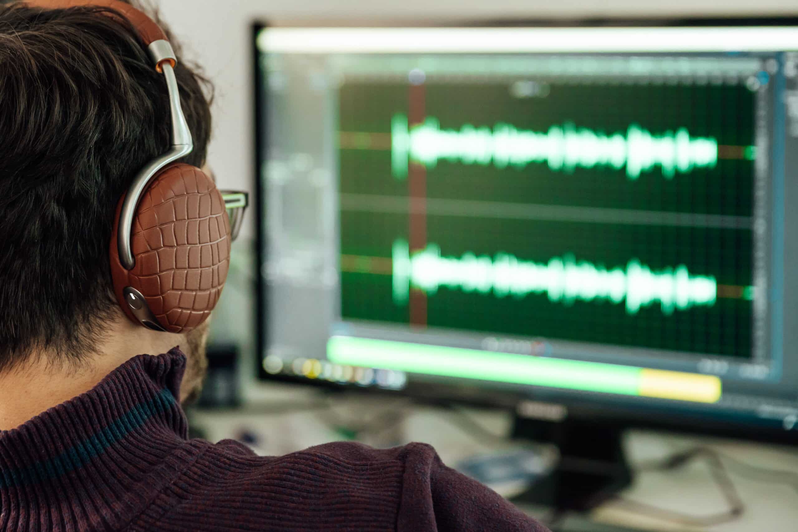 Primer plano de un diseñador de sonido ajustando una onda de audio en una pantalla, en pleno proceso de creación de un audio logo y una identidad sonora de marca.