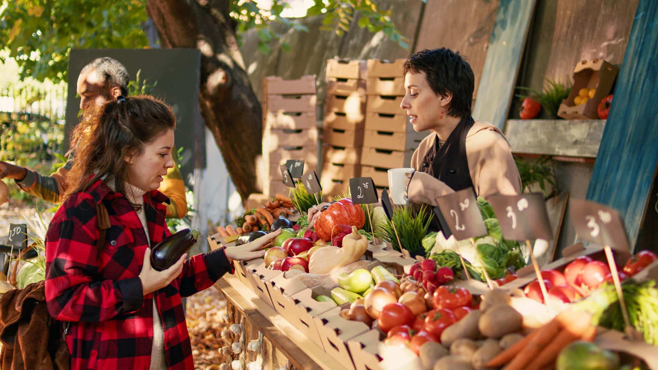 Una viajera sonriendo mientras compra fruta fresca directamente a un agricultor en un pequeño mercado local, ilustrando un branding sostenible y un customer journey que apoya la economía y cultura locales.