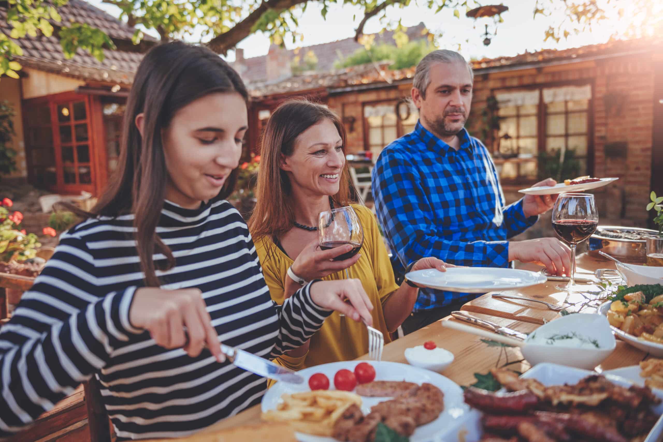 Un grupo diverso de personas compartiendo una comida y risas en una larga mesa de madera en un patio español, representando la narrativa de marca del slow travel que se centra en experiencias auténticas y conexiones humanas.