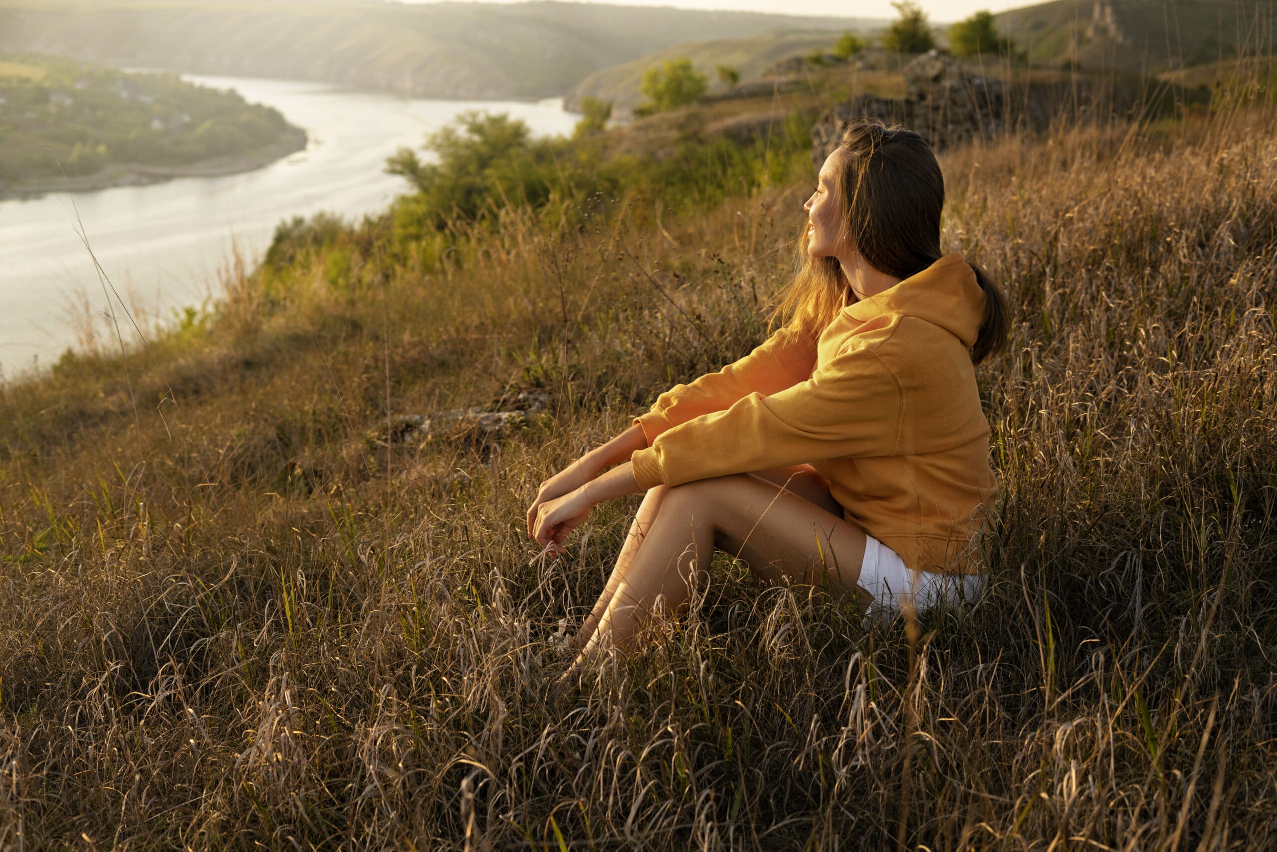 Viajera practicando slow travel, sentada en una colina y contemplando un valle sereno al atardecer, simbolizando la conexión profunda con el destino que define a una slow brand.