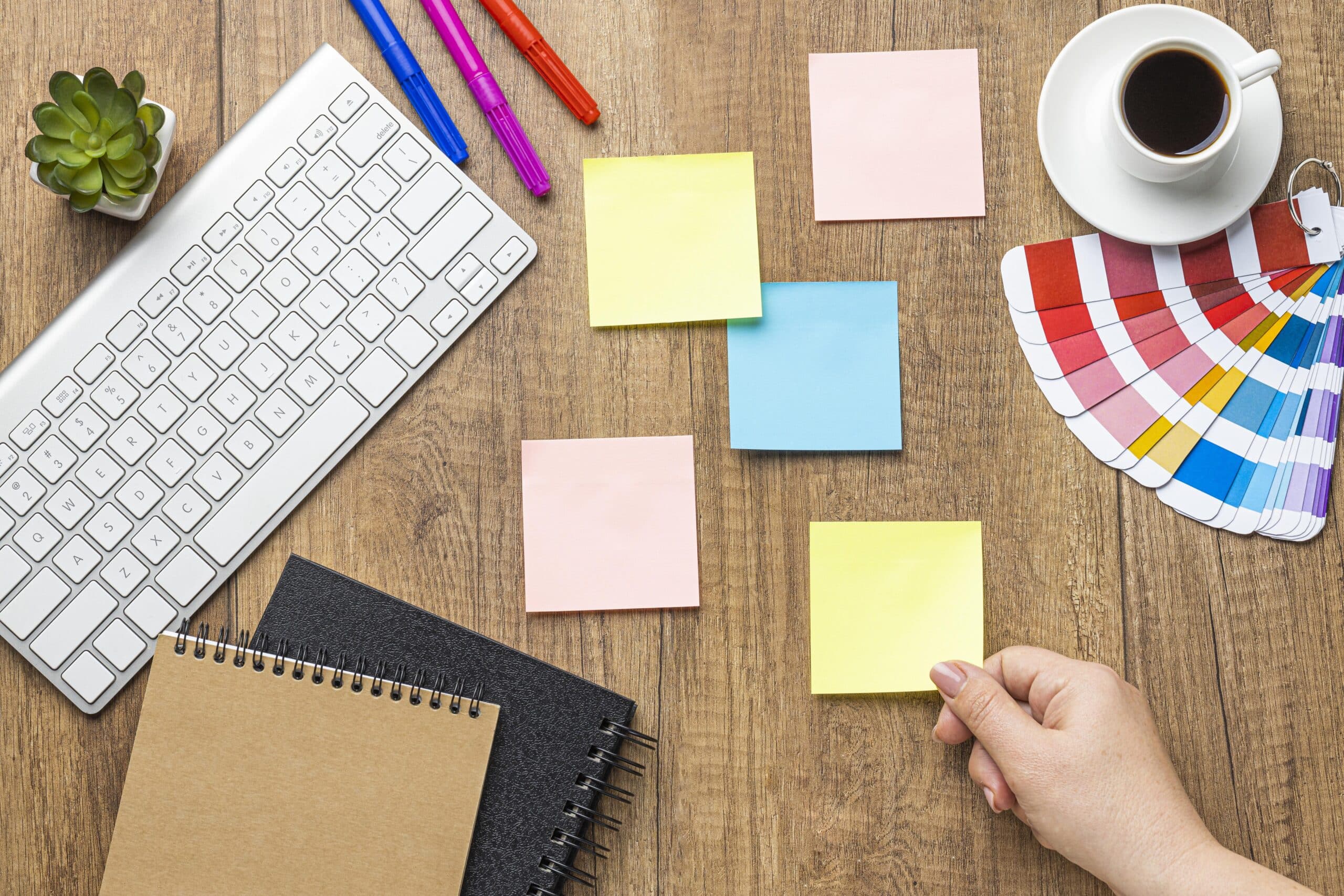 Escritorio de trabajo con herramientas para definir el tono de voz de una marca: libreta con un mapa conceptual, post-its y paleta de colores.